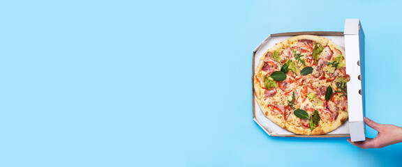 female hand open a package of pizza on a blue background. Top view, flat lay. Banner