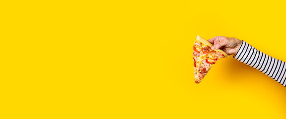 female hand holds a slice of fresh hot pizza on a yellow background. Banner