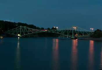 Long exposure landscape of old, green metal bridge at night. Smooth blue water.