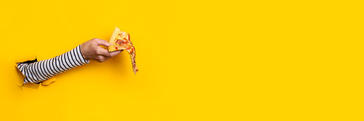 female hand holds a slice of fresh hot pizza on a torn yellow background. Banner