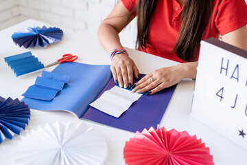 Beautiful woman making DIY paper fans of red and blue colors, celebrating Independence day of the...