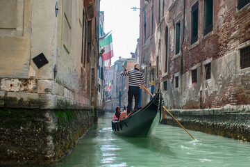 Naklejka na ściany i meble San Marco / Venice / Italy - April 17, 2019: Tourists in gondola ride in the historic city of Venice in Italy. Small canal
