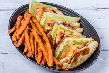A serving of club sandwiches cut into triangles with sweet potato fries on the side