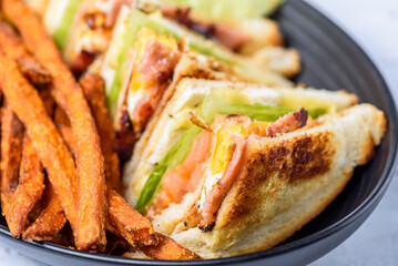 A serving of club sandwiches cut into triangles with sweet potato fries on the side