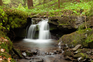 Une pause longue d´un petit ruisseau coulant au milieu de la forêt. Des rochers encadrent le ruisseau. Il y a une ambiance féérique.
