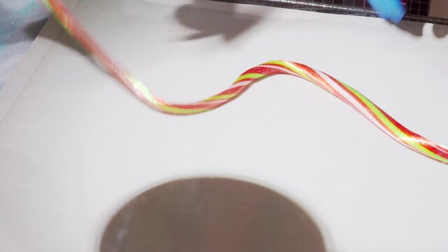 Confectioners making candies from melted colored sugar by rolling and cutting in candy workshop. Two hands making long candy bar on table. Colorful sweets making by japanese chef. 
