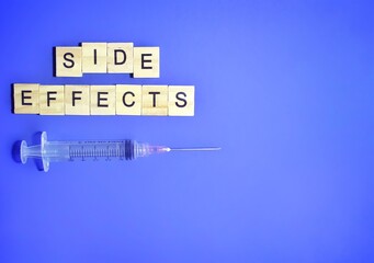 Top view of medical syringe and wooden cube with text SIDE EFFECTS on blue background. Copy space for text