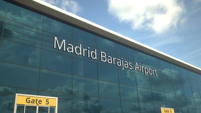 Landing airplane reflects in the modern windows with Madrid Barajas Airport text