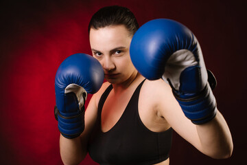 Extreme sport woman boxer wearing blue boxing gloves on dark red background