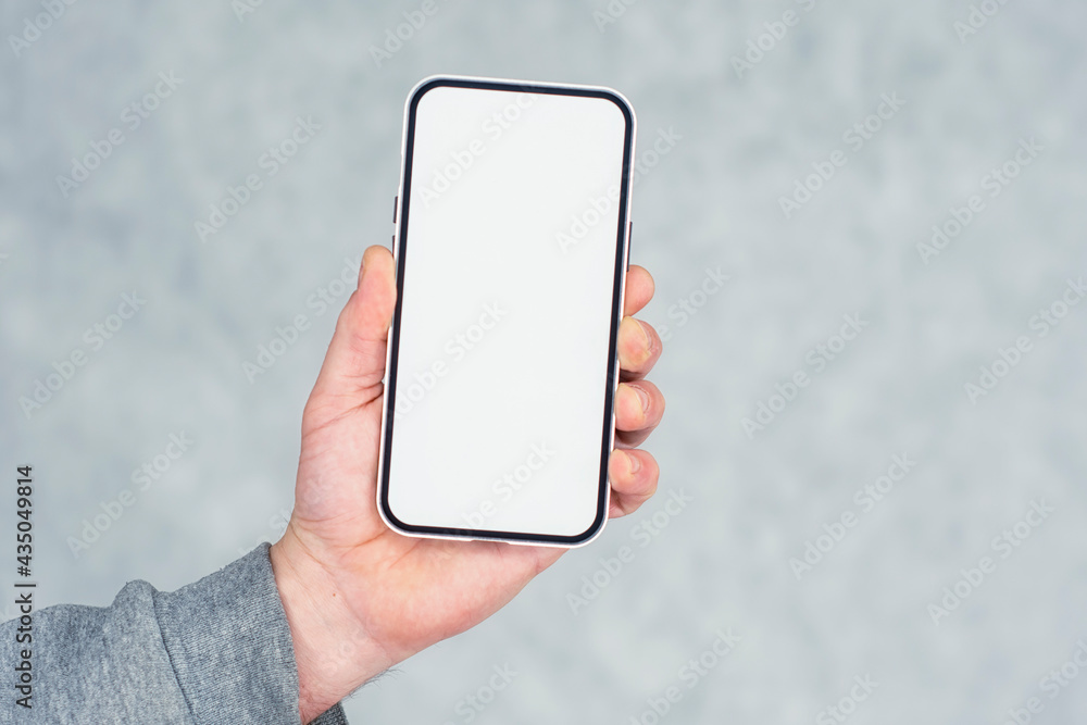 Aufkleber man in a gray sweater holds a mock-up of a smartphone with a white screen close-up on a light backgr