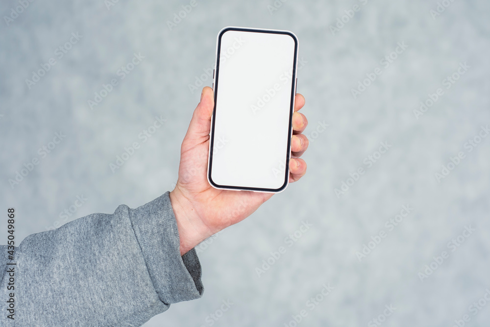 Poster man in a gray sweater holds a mock-up of a smartphone with a white screen close-up on a light backgr