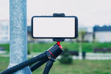 Mock-up of a smartphone with a white screen on a tripod outdoors.