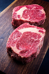 Modern Style rohes dry aged Wagyu Rib-Eye Beef Steaks angeboten als close-up auf einem Design Holz Board mit Textfreiraum