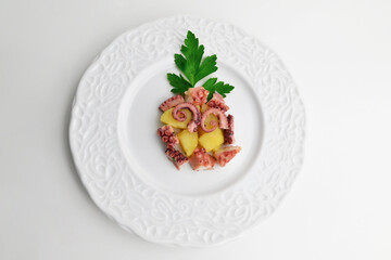 Warm salad with octopus, potatoes, tomatoes and lemon on a white plate. Close-up, white background. Top view.