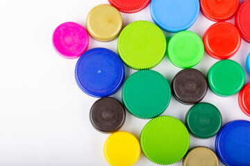 Many multi-colored plastic bottle caps on a white background.
