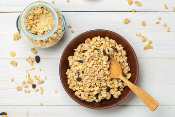 Healthy breakfast. Muesli with dried grapes in a clay bowl on a white wooden table. Muesli is scattered on the table. Space for text.