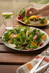 Summer sunny meal with big plate of salad with greens, reddish, eggs, olives. A woman takes a a basil from a plate with vegetables.