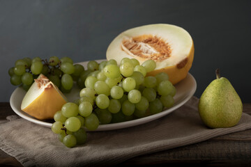 White plate with melon and grape next to pear. Classic still life. Soft light.