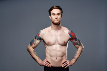 Fototapeta na wymiar handsome man with a naked pumped-up torso tattoos on his arms holds his hands on his belt