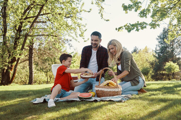 Happy young mother and father with little boy smiling while having picnic outdoors
