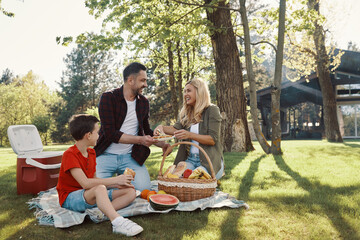 Happy young mother and father with little boy smiling while having picnic outdoors
