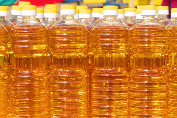 A row of transparent plastic bottles with edible vegetable on the market counter. The liquid has an oily appearance and an amber color. Background. Food.