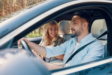 Happy young couple in casual wear smiling while driving in the car