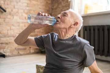 Fototapeta na wymiar Active elderly man drinking water after fitness workout at home