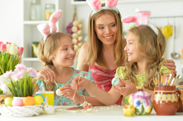 Obraz na płótnie Canvas Mother with daughters wearing rabbit ears decorating Easter eggs