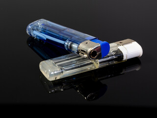 Two gas lighters in different colours on a black reflecting background