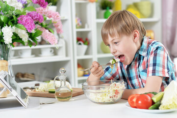 Cute boy eating  salad on kitchen table at home