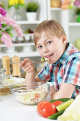 Cute boy eating  salad on kitchen table at home