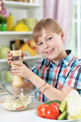 Cute boy preparing salad on kitchen table at home