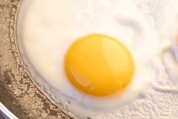 Cooked small fried eggs with finish white and bright round raw yolk in a dark skillet, Edge cracks. Simple breakfast. Top view, close-up