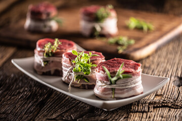 Raw steaks wrapped with bacon and fresh herbs on a plate and vintage wooden surface
