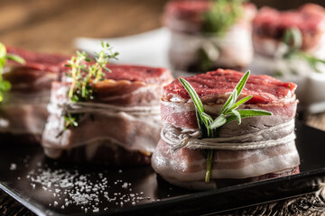 Raw steaks wrapped with bacon and fresh herbs on a plate and vintage wooden surface