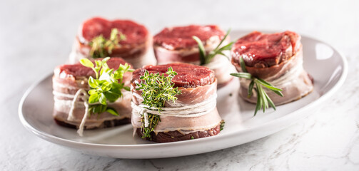 Raw steaks wrapped with bacon and fresh herbs on a plate