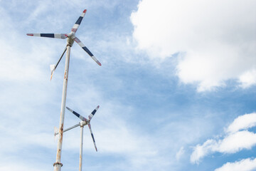 The side of a rusty metal stand of windwheels is spin in the blue sky.
