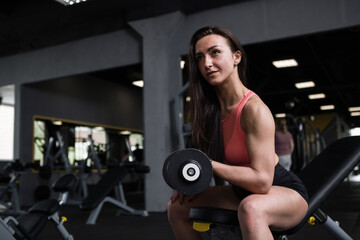 Fototapeta na wymiar Sportswoman with muscular arms doing biceps curls, at the gym, copy space