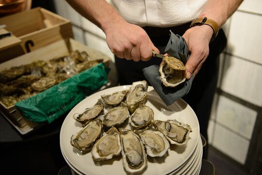 Man with knife openin oyster. Many oysters visible. Box of oysters in background