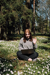 Woman with a laptop in the park. Young female sitting in grass with flowers work remotely in nature. Work everywhere travel blogger outdoors. Businesswoman sitting in forest Remote working concept