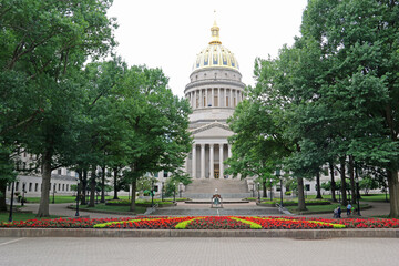 The West Virginia Capitol glows in the sun with the liberty bell in the foreground.