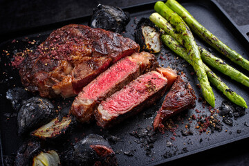 Modern style barbecue dry aged wagyu rib-eye beef steaks with green asparagus and charred onions...