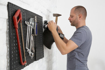 Man organizing his tools on the plastic pegboard on the wall in workshop.