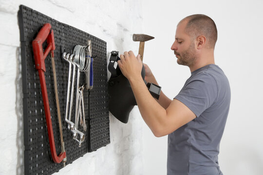 Man Organizing His Tools On The Plastic Pegboard On The Wall In Workshop.