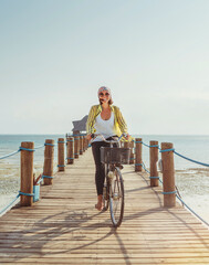 Portrait of a happy smiling woman dressed in light summer clothes and sunglasses riding a bicycle...