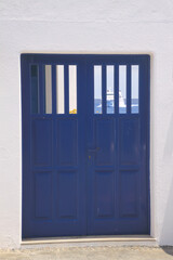 View on isolated mediterranean blue wood door with white wall. Blurred ferry boat and sea in window background.