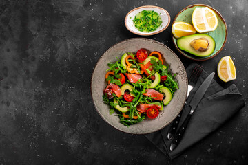 Fresh summer vegetable salad with arugula, tomatoes, bell peppers, avocado and salmon on a plate top view, photo with free space for text