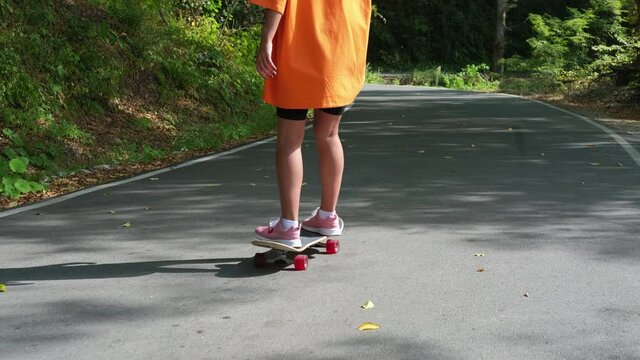 young sporty woman is skateboarding at summer, standing on board and rolling over road