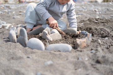 Child boy folds castle of stones, play with rocks on the shore on a sunny day.